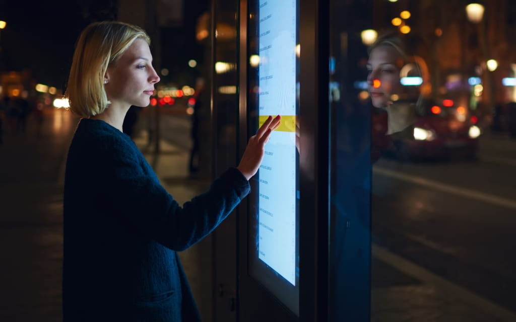 Eine Frau steht vor einer digitalen Tafel und bedient sie mit ihrem Finger
